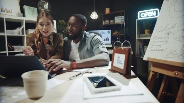 Friendly girl talking to afro guy about data on laptop screen in workplace. — Stock Video
