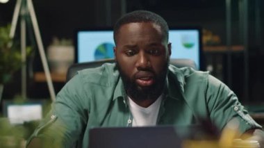 Üzgün afro işadamı ofiste kötü haberler okuyor. Bilgisayarda çalışan Afrikalı adam