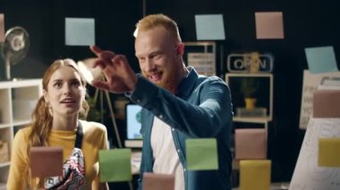 Kapalı kapılar ardında neşeli hipster çift gece ofisindeki cam levhalara bakıyor.