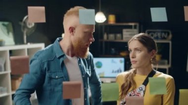 İş adamları hipster ofisindeki şeffaf duvardaki çıkartmalar hakkında tartışıyorlar.