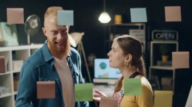 Genç iş ortakları hipster ofisindeki çıkartma tahtasında fikirleri tartışıyor..