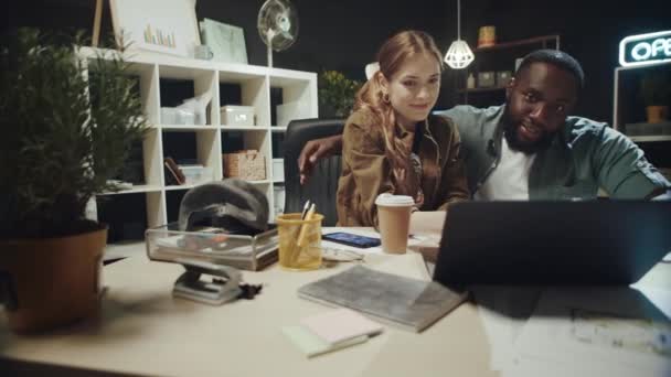 Flirter afro homme étreignant belle dame près d'un ordinateur portable dans le bureau hipster. — Video