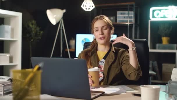 Mujer de negocios charlando en línea en el lugar de trabajo. Jovencita bebiendo café adentro. — Vídeos de Stock