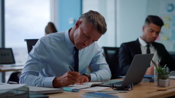 Hombre de negocios enfocado tomando notas en un cuaderno. Hombre empresario escribiendo en el ordenador portátil — Vídeos de Stock