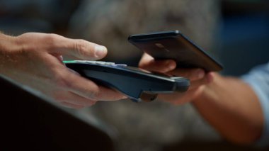 NFC teknolojisi ile pos terminali üzerinden cep telefonuyla ödeme yapan işadamı.