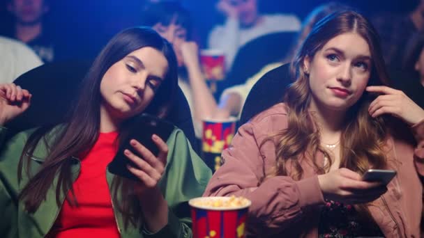 Donne sconvolte che controllano il cellulare al cinema. Ragazze smartphone scorrimento indoor. — Video Stock