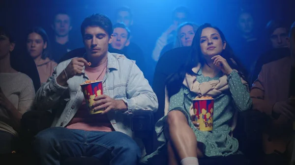 Young people eating popcorn in cinema. Attractive couple watching movie in hall. — Stock Photo, Image