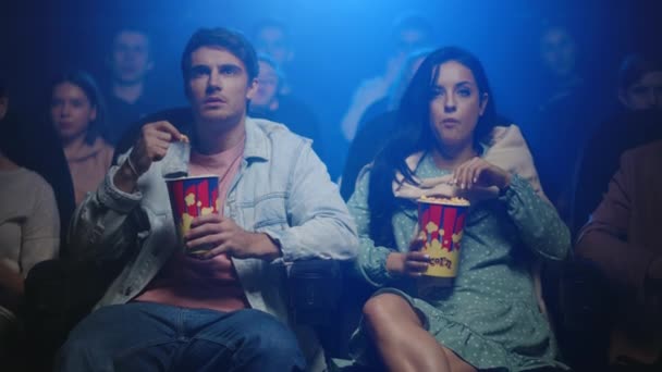 Jóvenes sorprendentes en el cine. Atractiva pareja viendo películas en el hall oscuro. — Vídeos de Stock