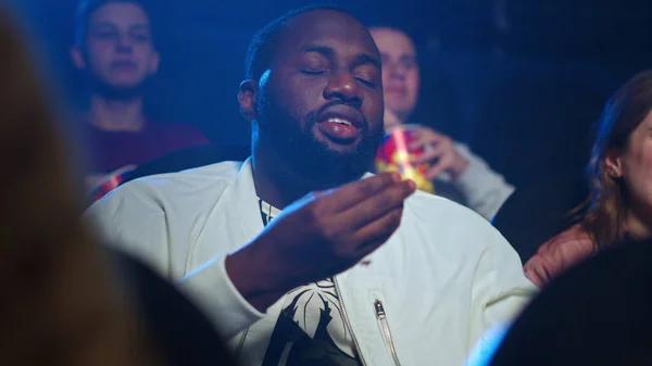 African man eating popcorn in movie theater. Afro guy laughing in cinema.