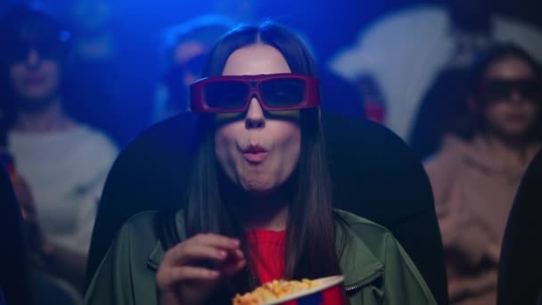 Uma mulher assustada a ver filmes no cinema. Menina em óculos 3d comer pipoca — Vídeo de Stock