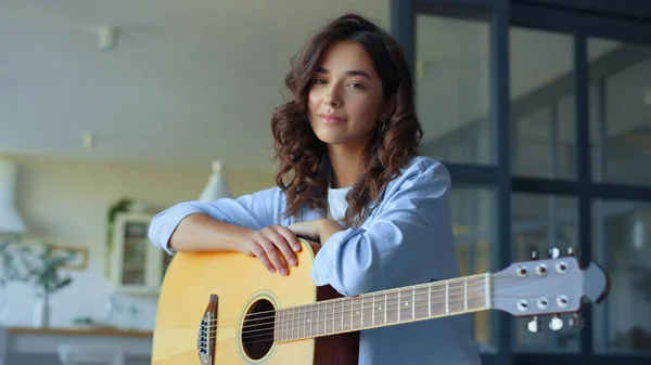 Drömmande tjej med akustisk gitarr hemma. Lycklig kvinna tittar på kameran — Stockfoto
