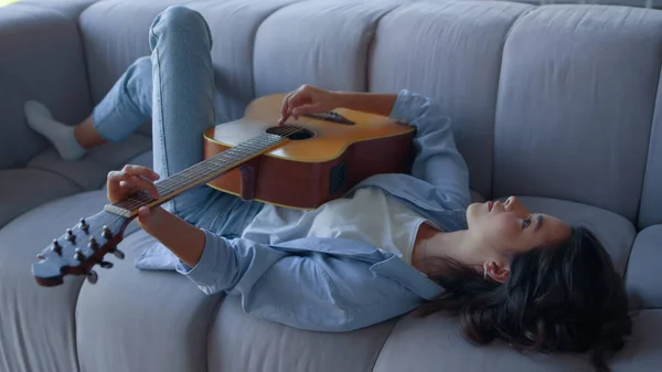Hon spelar gitarr på soffan. Avslappnad musiker spelar ackord på akustisk gitarr — Stockfoto
