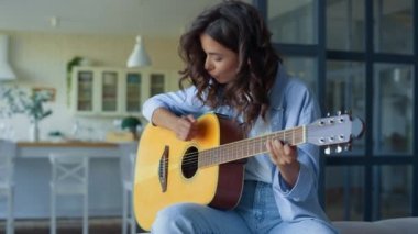 Evde gitar çalan bir kız. Mutlu kadın telli çalgılarla müzik çalışıyor.