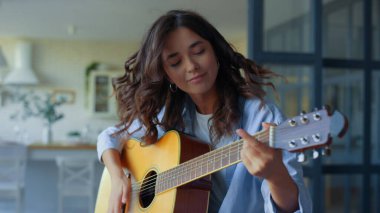 Oturma odasında gitar çalan bir kız. İp enstrümanında müzisyen akorları
