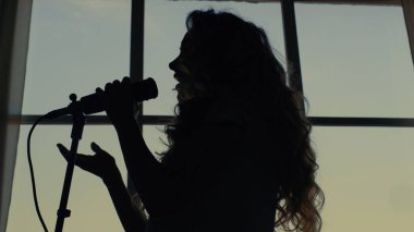 Kadın mikrofonda şarkı söylüyor. Şarkıcı mikrofonla şarkı söylüyor