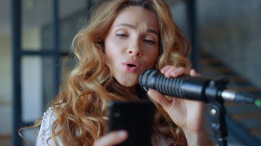 Vokalist mikrofonda şarkı söylüyor. Akıllı telefondan şarkı metni öğrenen odaklı kadın