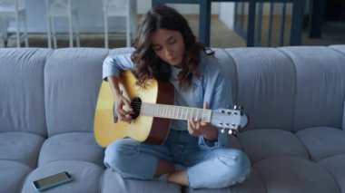 Evde gitar çalmayı öğrenmeye odaklanmış bir kız. Gitar çalan genç bir kadın