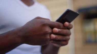 Bilinmeyen afro bir adam sokakta mesaj yolluyor. Afrikalı erkek elleri cep telefonuyla