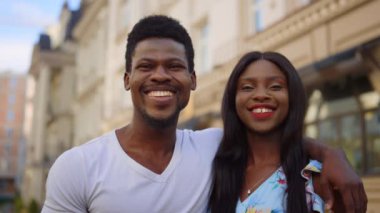 Şehirde objektife bakan gülümseyen bir çift. Sokakta kameraya bakan Afro insanlar