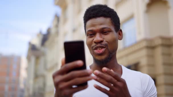Взволнованный афро-парень с видеозвонком на улице. Человек делает жест рукой на открытом воздухе — стоковое видео
