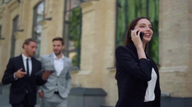 Dışarıda cep telefonu kullanan gülümseyen bir kadın. İş adamları işi aceleye getiriyor.