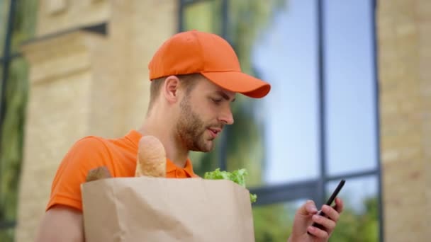 Corriere che utilizza il telefono cellulare per l'indirizzo di ricerca. Uomo che consegna cibo in borsa. — Video Stock