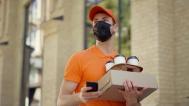 Maskeli kurye dışarıda akıllı telefon kullanıyor. Siparişleri taşıyan teslimatçı..