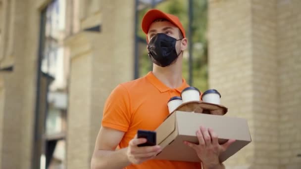 Maskerkoerier met smartphone buiten. Leverancier draagt bestelling buiten. — Stockvideo