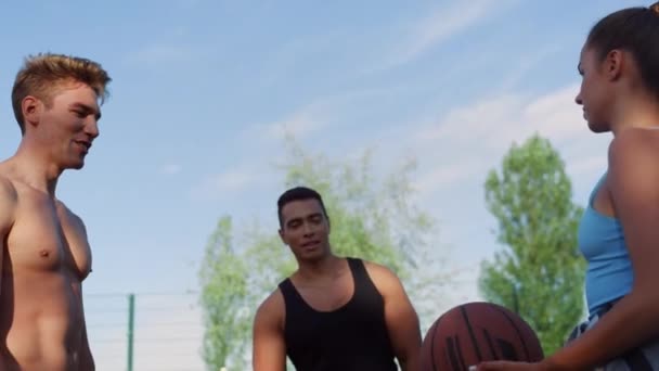 Tre giocatori misti che allenano il basket di strada nel parco giochi sportivo. — Video Stock