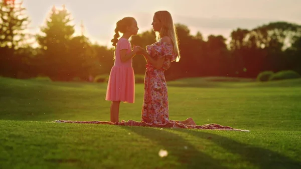 妈妈在城市公园拥抱女儿。黎明时分在草地上与女孩交谈的女人 — 图库照片