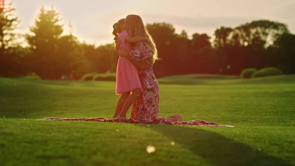 Kvinna och flicka njuter av soluppgången i trädgården. Mor kramar dotter i stadsparken. — Stockfoto