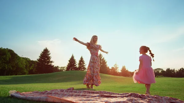 Szczęśliwa matka tańcząca z córką na trawie. Dziewczyna robi gwiazdę w parku. — Zdjęcie stockowe