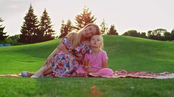 Famille posant au coucher du soleil au pré. Femme câlin fille dans la ville parc. — Photo