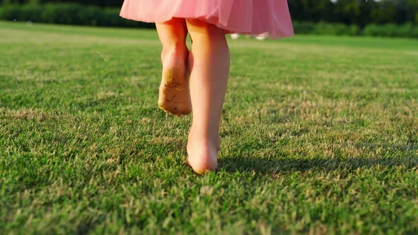 Вид сзади на неузнаваемую девушку, бегущую босиком по зеленой траве в городском парке. — стоковое фото