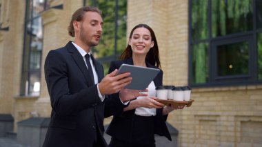 İş arkadaşları giderken tartışıyorlar. Tablet ve kahveyle yürüyen insanlar.