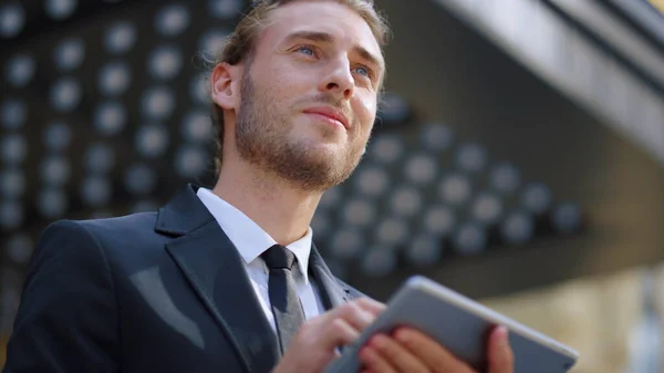 Sly businessman smiling someone outside. Serious guy using tablet outdoors