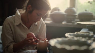 Çömlekçilikte el işi yapan genç bir seramistim. Kadın ürünlere süs takıyor.