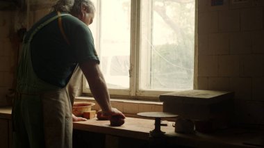 Ciddi bir adam atölyedeki el işi dersine hazırlanıyor. Seramikçi kil heykeli