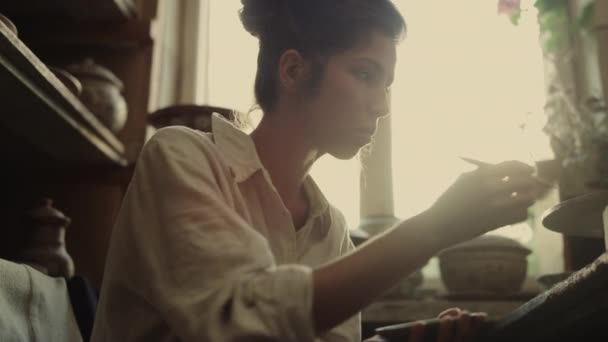 Сосредоточенная девушка украшает тарелку в студии. Женщина, работающая с мокрой глиной в керамике — стоковое видео