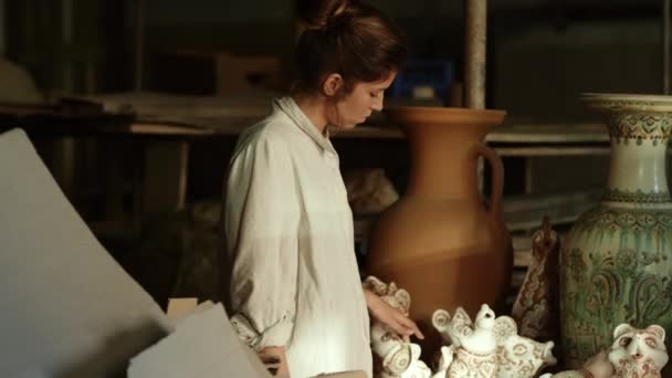 Συγκεντρωμένη κυρία που περπατάει σε στούντιο γεμάτο κεραμικά. Γυναίκα που εξετάζει προϊόντα — Αρχείο Βίντεο