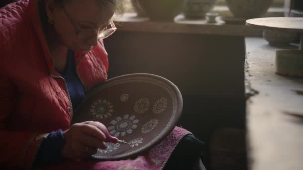 Seniorin zeichnet Tonteller in Keramik. Künstler fertigt Ornament in Werkstatt — Stockvideo