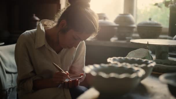 Schöne Frau, die Schmuck auf einem Produkt aus Keramik herstellt. Mädchen zeichnen auf nassem Ton — Stockvideo