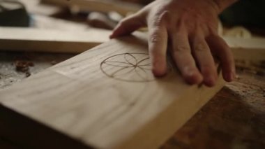 Tanımlanamayan adam içeride ahşap desen çiziyor. Marangoz ürünü bitiriyor.