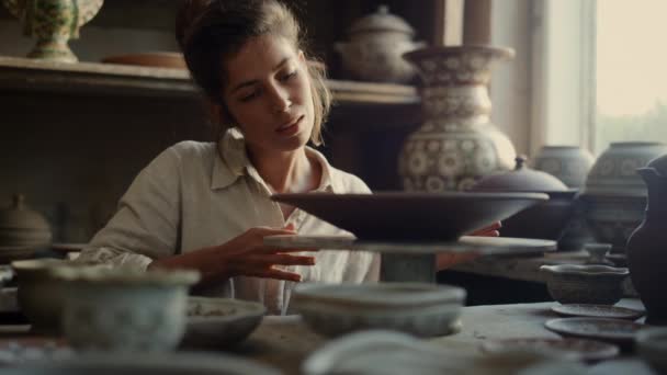 Улыбающаяся леди касается тарелки в керамике. Художник наслаждается глиной в мастерской — стоковое видео