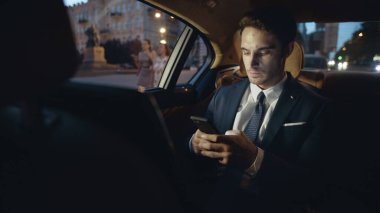 İş adamı arabada akıllı telefondan mesaj yazıyor. Cep telefonunda metin yazan adam