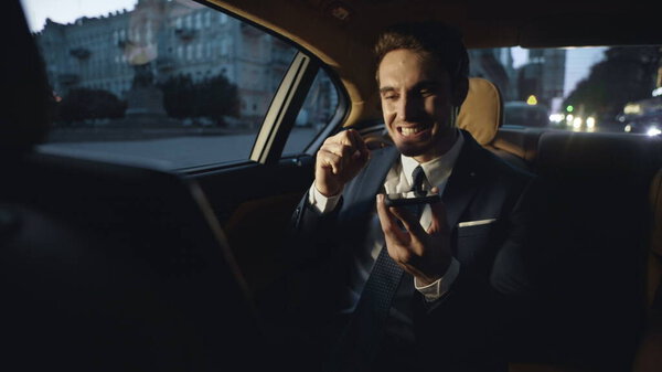 Разгневанный бизнесмен ругается в голосовом чате на мобильном телефоне в тёмной машине.