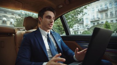 İş adamı laptopta arabada görüntülü konuşma yapıyor. Video mesajı kaydeden adam