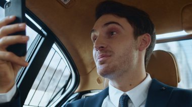 Gülümseyen işadamı modern arabadaki akıllı telefondan görüntülü sohbette iyi haberler veriyor..