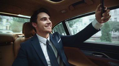 Gülümseyen iş adamı iş arabasında akıllı telefondan selfie çekiyor..