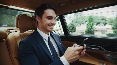 Neşeli iş adamı lüks arabasıyla akıllı telefondan mesaj yazıyor..